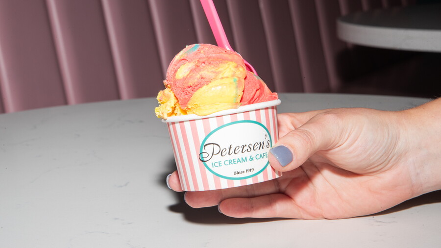 A hand holding a striped Petersen's cup of Superman ice cream at a shop table.